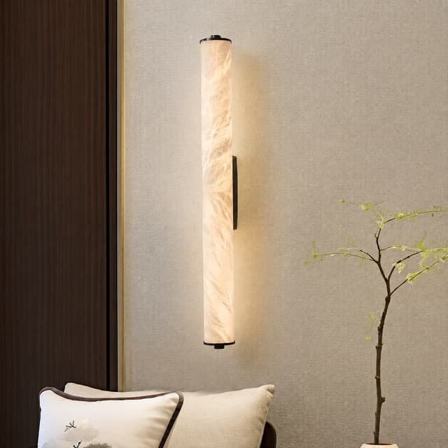 Vertical translucent stone look wall sconce beside a lounge chair and indoor plant