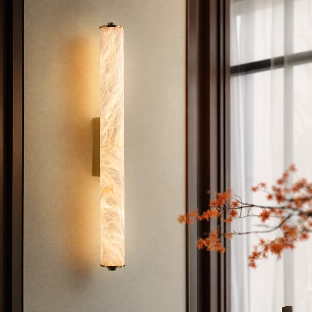 Brass vertical cylinder wall sconce with warm diffused light beside a window