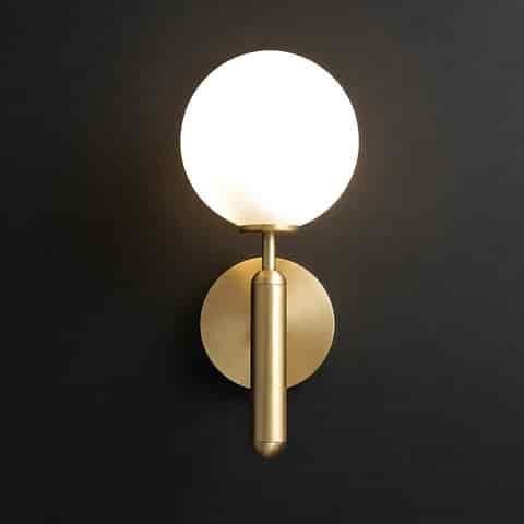 Modern brass finish globe wall sconce with frosted glass shade on a dark textured wall