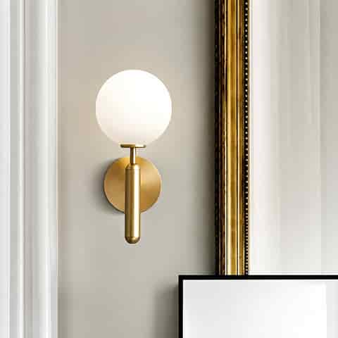 Minimalist brass globe wall sconce styled in a modern interior beside framed wall art