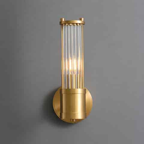 Single vertical brass finish glass rod wall sconce glowing on a gray wall