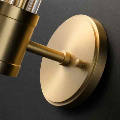 Close up of brushed brass finish round backplate and arm on a glass rod wall sconce
