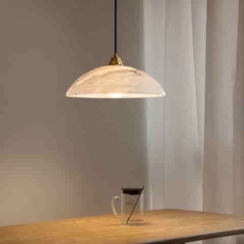 Natural alabaster dome pendant light with warm brass tone fitting above a modern dining table