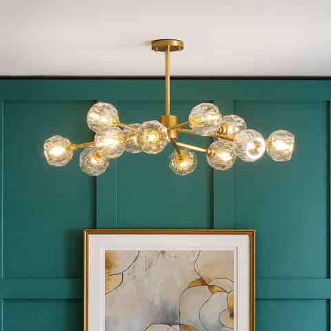 Gold branch chandelier with faceted clear globes installed against a teal paneled wall