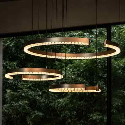 Graphite gray spiral LED chandeliers in different sizes suspended in front of large windows with warm ambient lighting