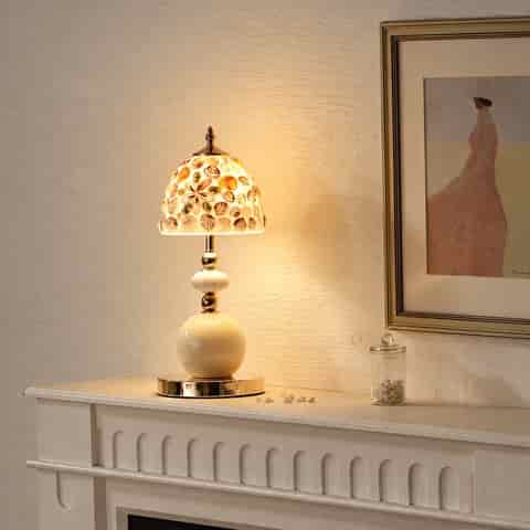 Ivory and gold seashell table lamp styled on a classic white mantel with a glowing shell and glass shade