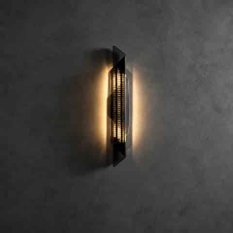 Black geometric LED wall sconce casting a warm decorative glow on a dark textured wall