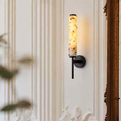 Blackened brass and terrazzo wall sconce with warm glow in a classic interior