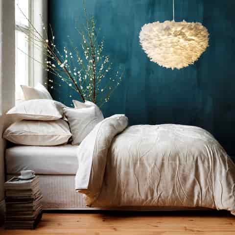 White feather pendant light in a cozy bedroom with teal accent wall and white bedding